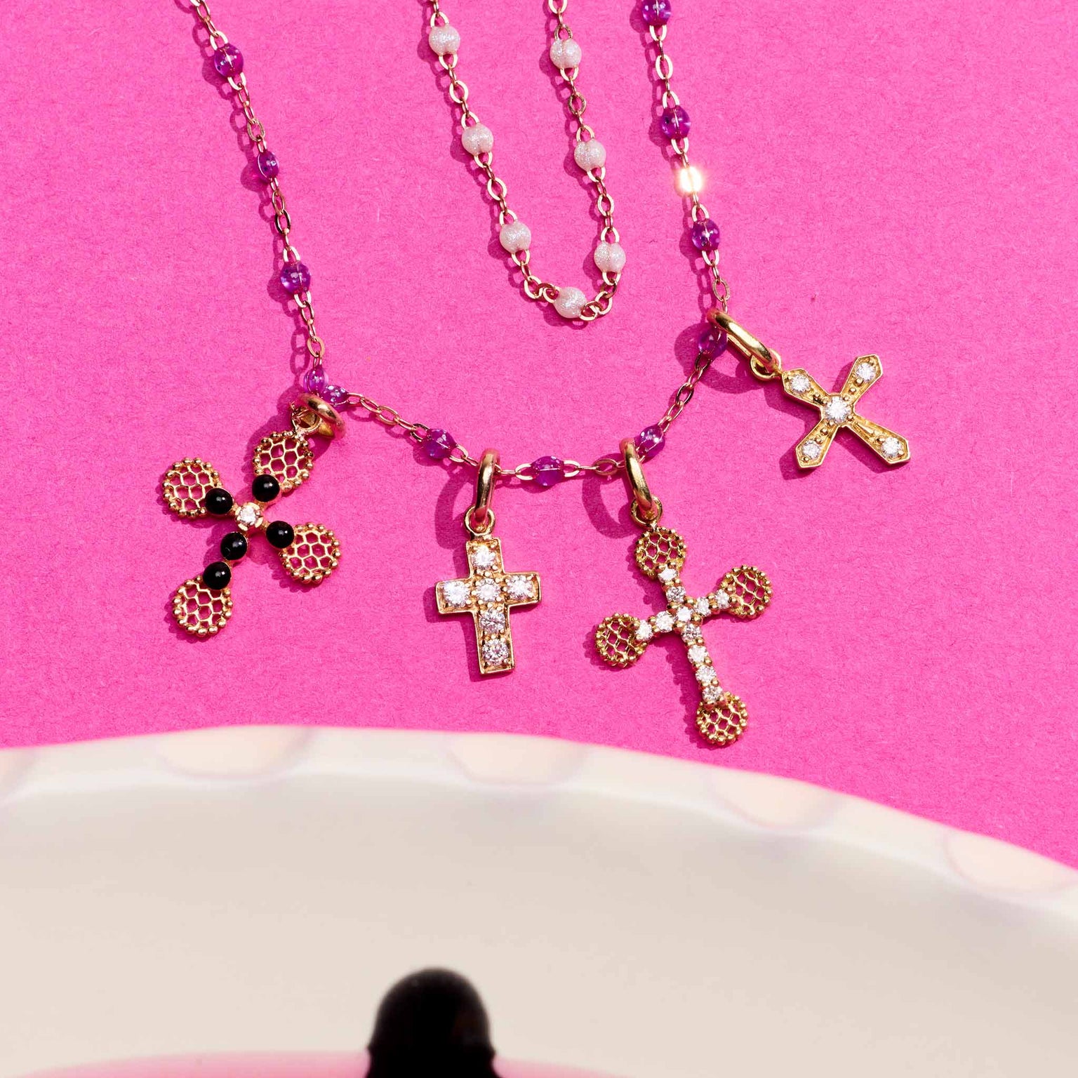 Photo de différent pendentifs croix Gigi Clozeau posé sur un fond rose 