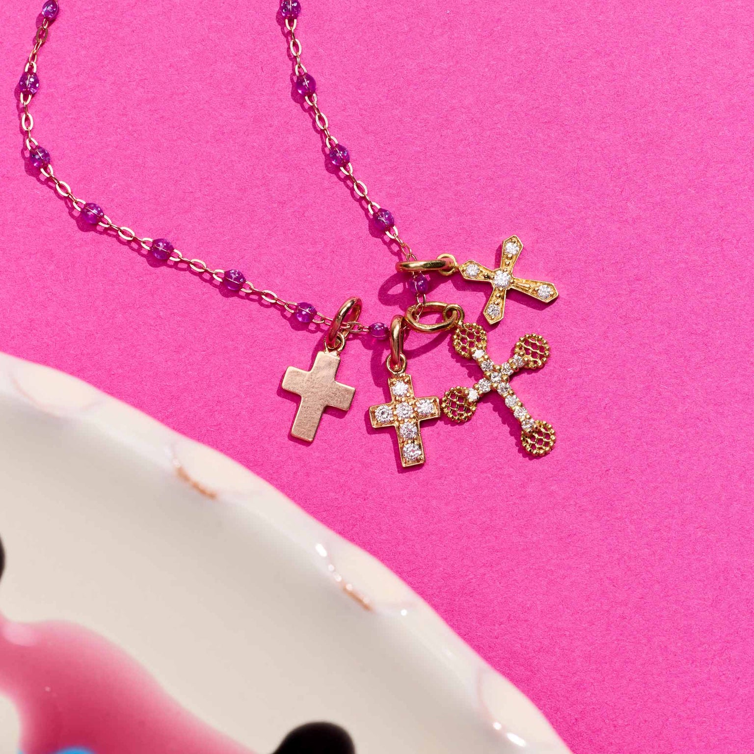 Photo de différent pendentifs croix Gigi Clozeau posé sur un fond rose 